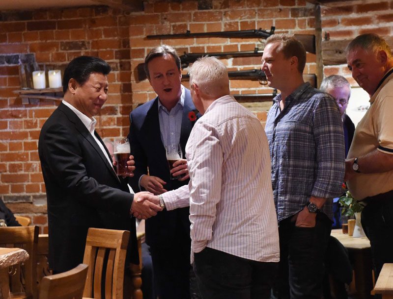 這是習近平與卡梅倫飲啤酒，並同當?shù)孛癖娊徽?。新華社記者 饒愛民 攝